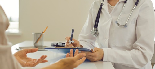 Someone in a white coat with a clipboard talking to another person (close up).