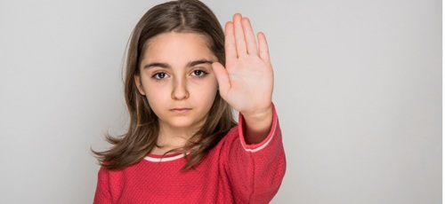 A young girl, staring at the camera, hand raised to say 'stop'.
