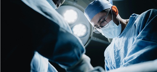 Up close shot of a surgeon's face in surgery, from below. With operating lights in the background