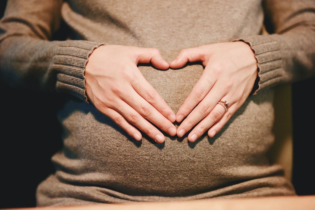 Pregnant woman's torso with hands on tummy forming a love heart